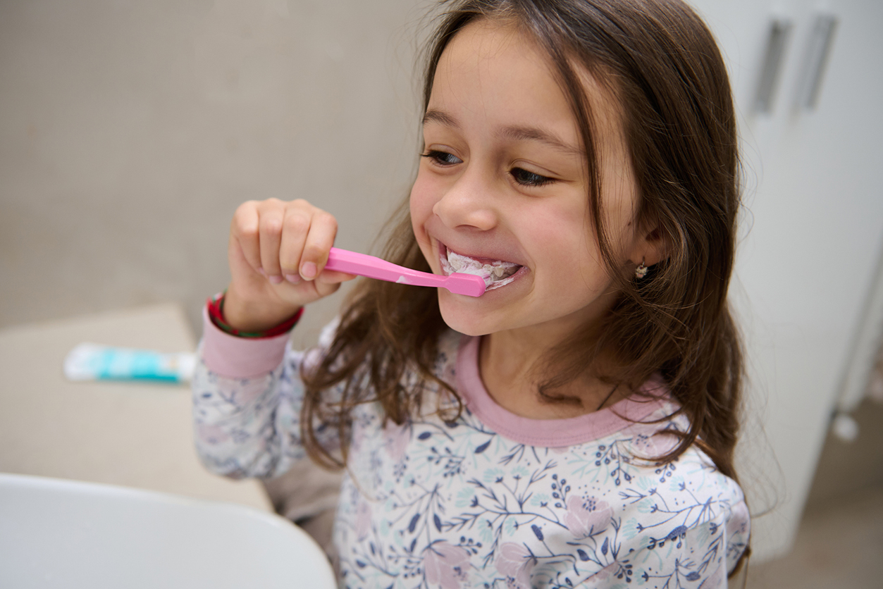 Post-Halloween Dental Check-Up - Adorable little child girl in pajamas, holding a toothbrush with toothpaste and brushing her white teeth in front of the mirror in the home bathroom. Healthy lifestyle. Dental oral care and hygiene