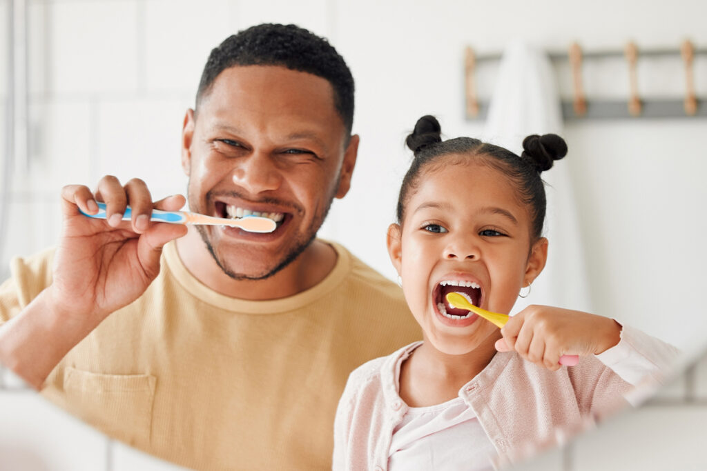 father and daughter brushing their teeth together in a bathroom at home.