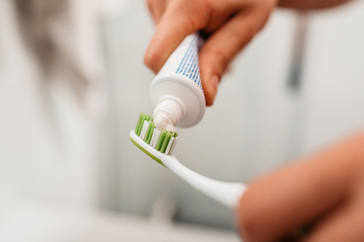 Close-up of person putting on toothpaste on a toothbrush to brush his teeth in the bathroom in the morning.