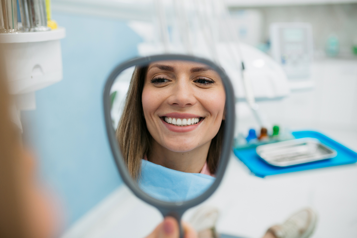 Teeth Whitening in Plymouth - A happy woman looking herself in the hand held mirror