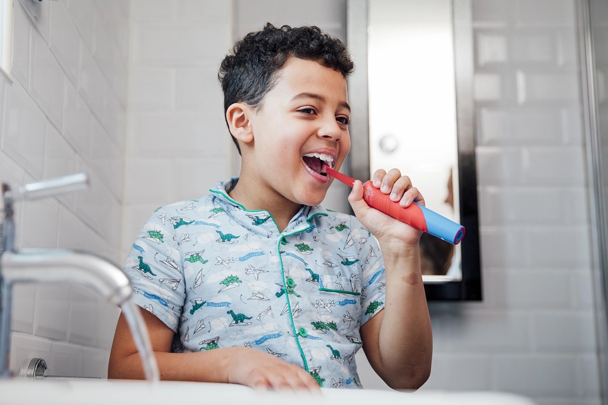 Best Toothbrush for Kids - child boy sitting next to sink brushing teeth with electric toothbrush