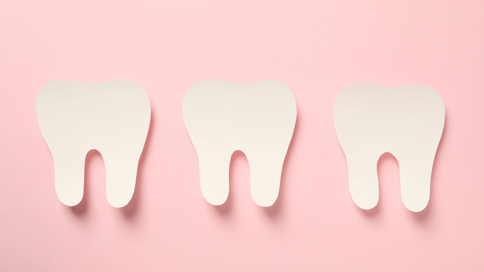 Three white tooth-shaped cutouts on a pink background, symbolizing dental health and enamel care