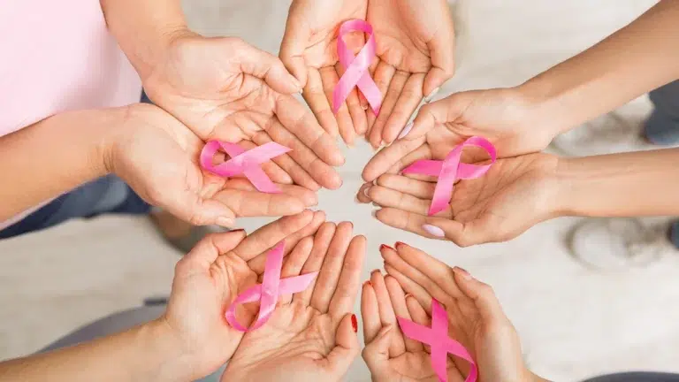 Hands holding pink ribbons in a circle, symbolizing community support and breast cancer awareness