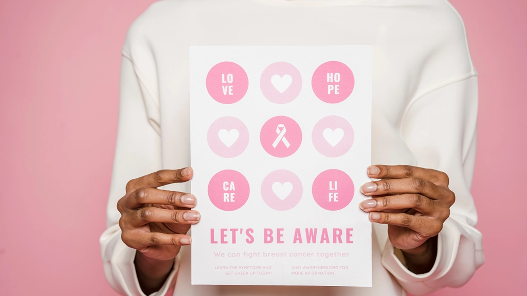 Close-up of a person holding a breast cancer awareness flyer with icons for love, hope, care, and life