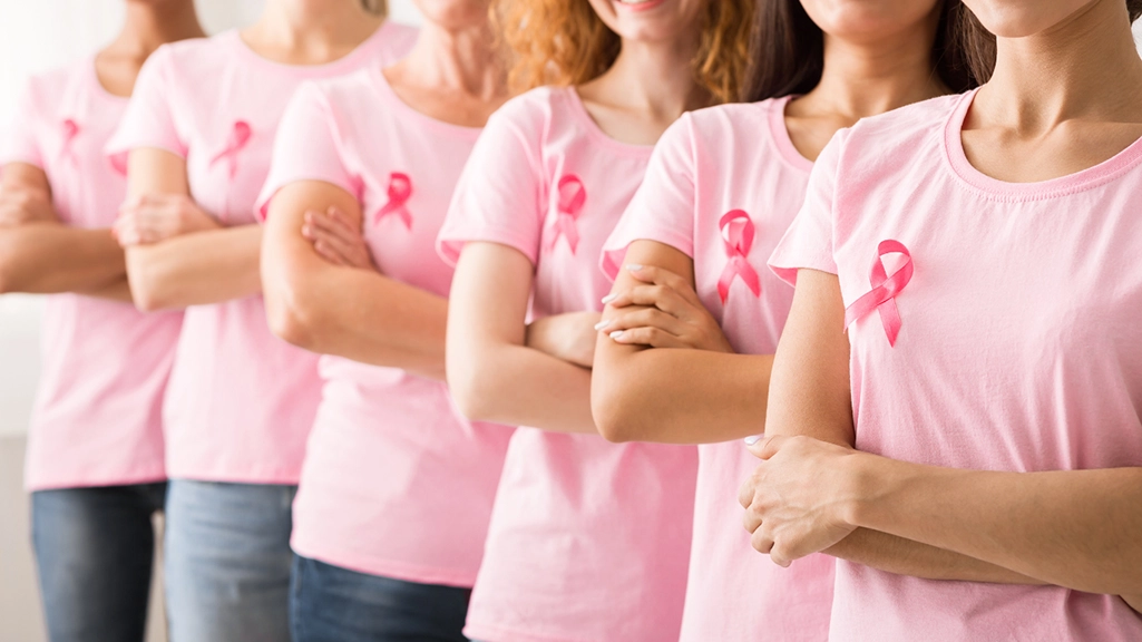 Women standing together wearing pink shirts and breast cancer ribbons, showing solidarity