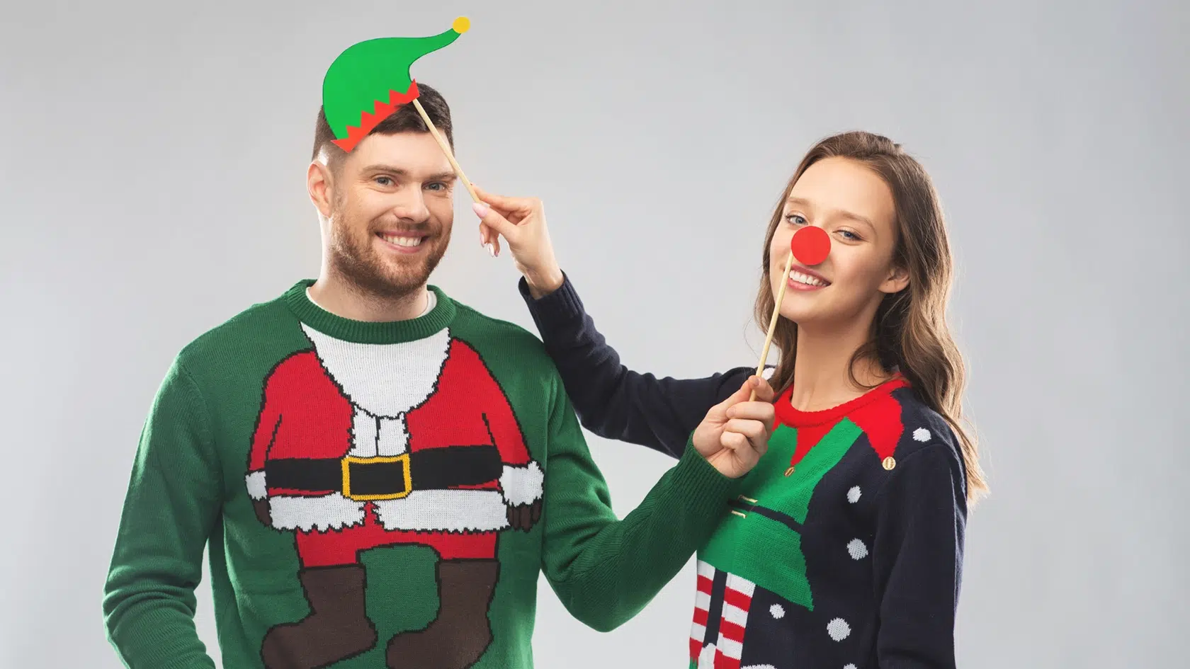 Couple wearing christmas sweaters being silly having given each other cosmetic dentistry for gifts