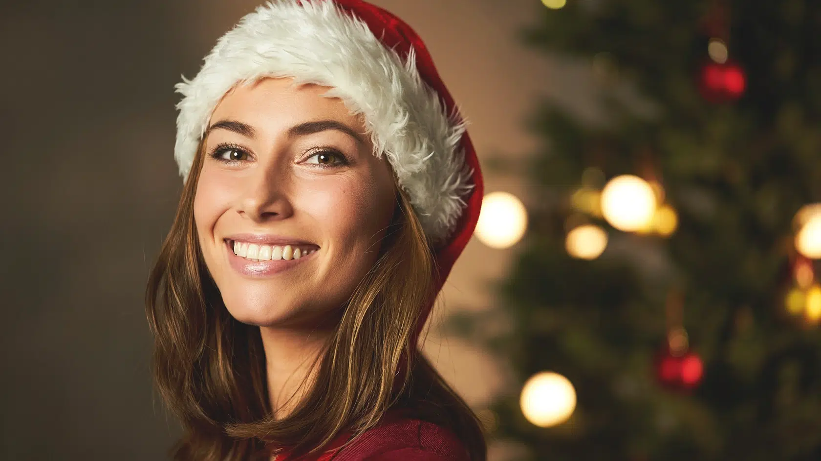 Woman wearing Santa hat smiling after professional teeth whitening