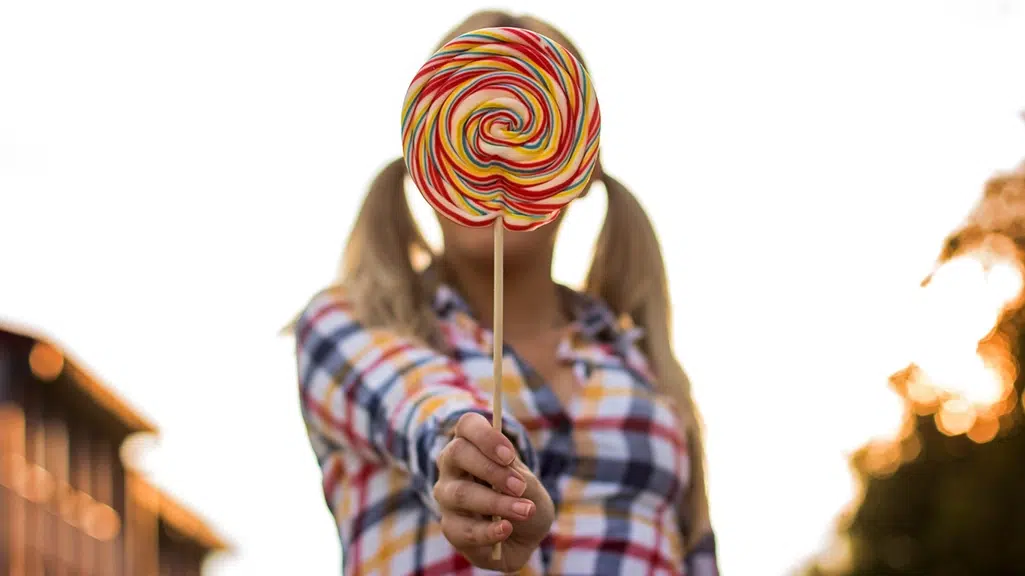 Woman holding large lollipop in front of her face showing foods to avoid for your tooth health