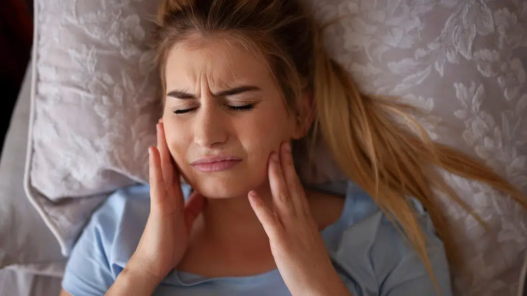 Woman hold jaw in pain in bed due to tooth pain interrupting her sleep