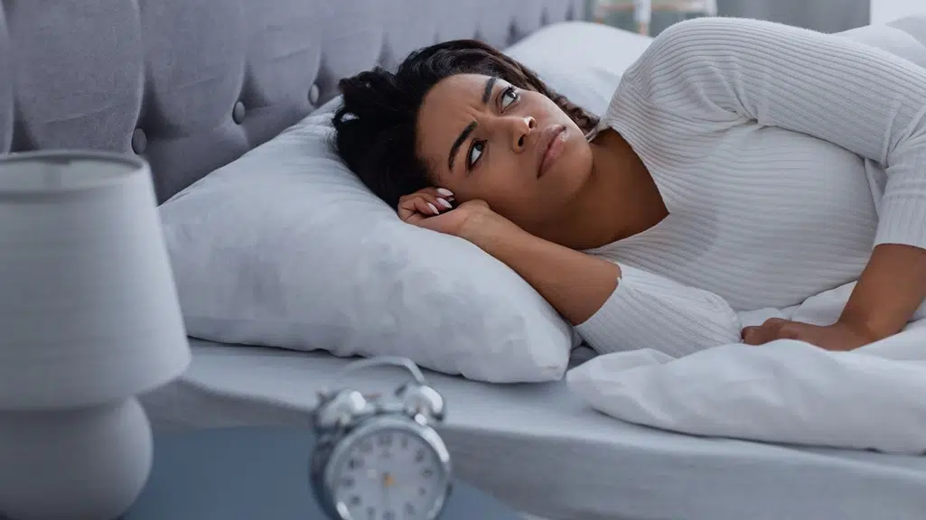 Woman lying awake in bed representing jaw pain or teeth grinding that can interfere with sleep