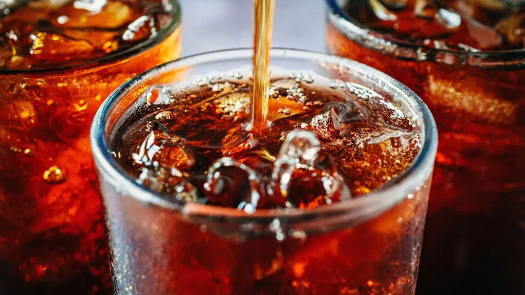 Cola soda being poured into glass over ice