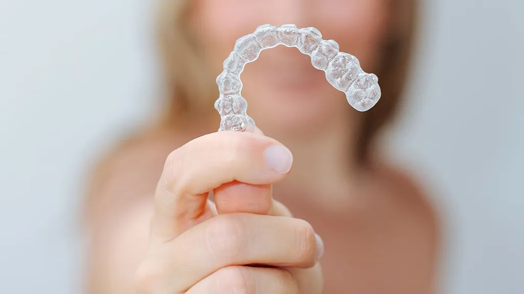 Clear Invisalign-style dental aligner held in front of a patient