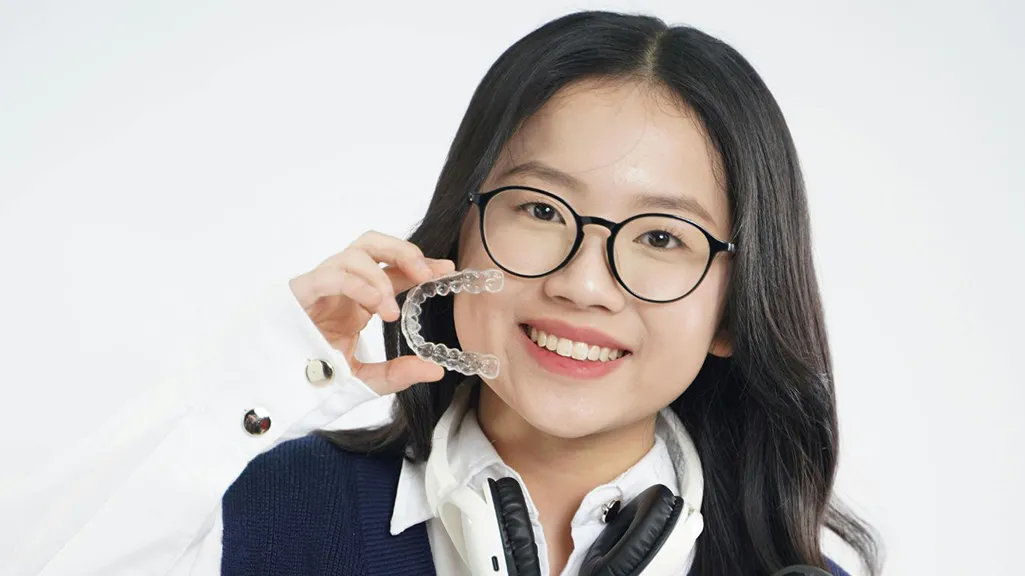 Teen holding a clear dental aligner and smiling